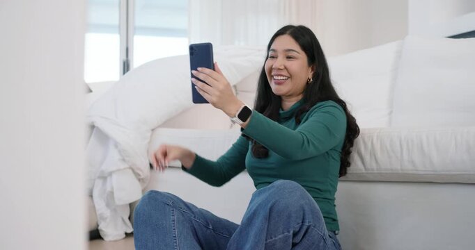 Cam reframing adult woman sitting on floor holding phone showing key while unpacking near sofa