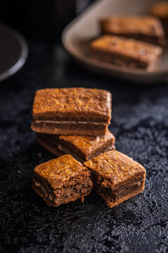 Close-Up Stack Of Chewy Chocolate Brownies With Crumbly Texture On Dark Surface