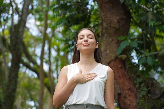 Front view of a mindful young woman with one hand on her heart and her eyes closed, breathing deeply in a Brazilian forest