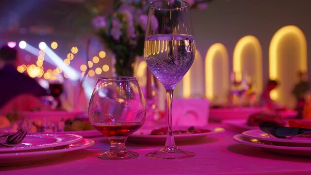 Sparkling champagne flute beside cognac snifter on table. Purple party lighting in banquet hall