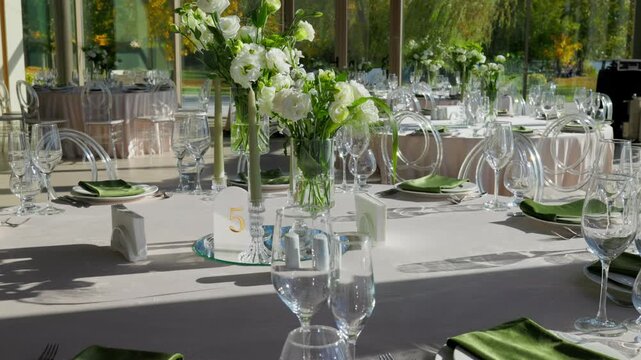 Table number five with white floral centerpiece and green napkins. Sunlit wedding banquet hall