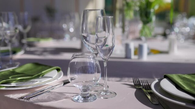 Crystal glassware and green cloth napkins on white plates. Formal restaurant table place setting