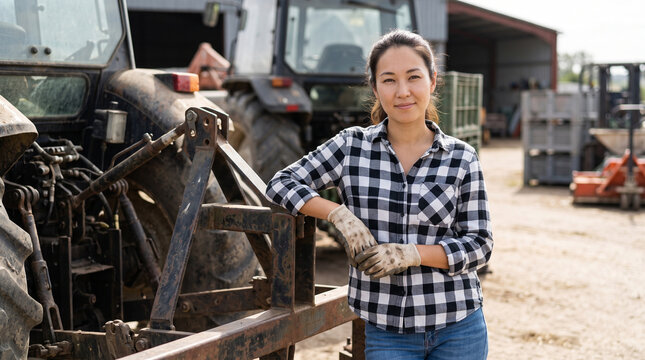 Female farmer leaning against agricultural machinery in a farmyard