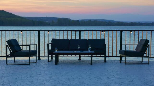 Twilight patio lounge with wineglasses and string lights. Symmetrical view of lakeside deck