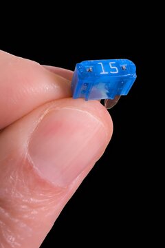 Close Up of Man Holding Blue 15 Amp Automotive Blade Fuse Against Black Background