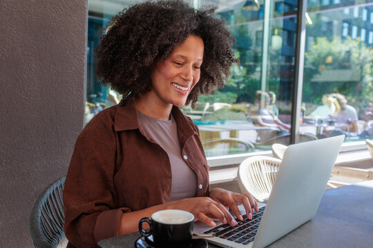 Digital nomad lifestyle, African woman working on laptop in a modern cafe