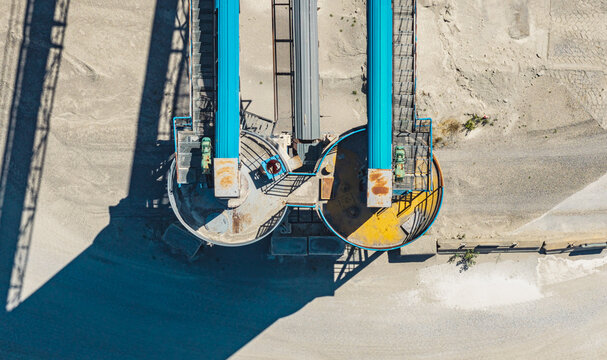 Aerial view of two parallel blue conveyor belts and circular machinery at a gravel processing facility, creating a symmetrical composition in Valence, Auvergne-Rhone-Alpes, France.
