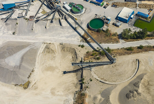 Aerial view of an aggregate processing facility with conveyor belts, sand and gravel stockpiles, water treatment tanks and industrial equipment in Valence, Auvergne-Rhone-Alpes, France.