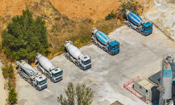 Aerial view of five concrete mixer trucks and a concrete pump truck parked at an industrial concrete batching plant in Valence, Auvergne-Rhone-Alpes, France.