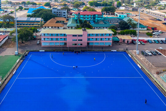 Aerial view of the National Hockey Pitch with its vibrant blue synthetic turf and surrounding buildings in Accra, Greater Accra Region, Ghana.