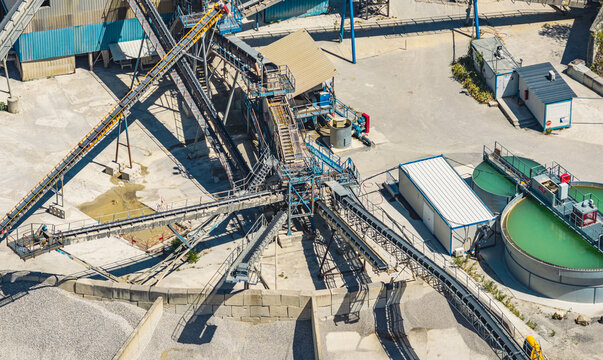 Aerial view of an industrial gravel processing plant featuring conveyor belts, screening equipment, steel platforms, and a circular water treatment tank in Valence, Auvergne-Rhone-Alpes, France.