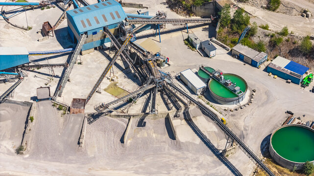 Aerial view of an industrial aggregate processing plant with conveyor belts, gravel screening machinery and circular water treatment tanks in Valence, Auvergne-Rhone-Alpes, France.