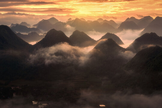 Aerial view of the limestone karst mountains of Bac Son valley shrouded in morning mist under a golden sunrise in Bac Son, Lang Son, Vietnam.