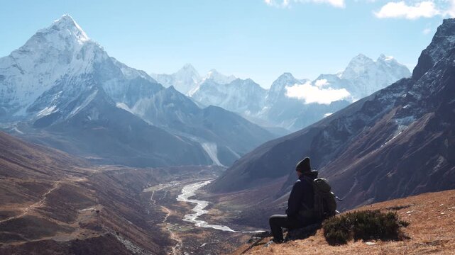 Hiker resting on top cliff, admiring breathtaking view himalayan mountain range with snow peak ama dablam. Deep valley and winding river in nepal. Hiker resting and enjoying view from top of mountain