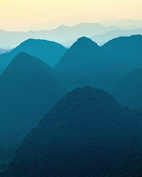 Aerial view of the lush green limestone karst mountains of Bac Son valley, with layers of peaks fading into the distance under a soft sunset sky in Bac Son, Lang Son, Vietnam.