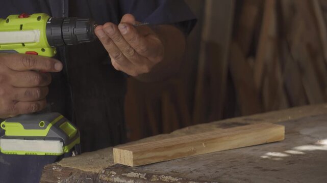 Close-up of a carpenter using a cordless electric drill to screw into a wooden plank in a woodworking workshop, handyman at work.