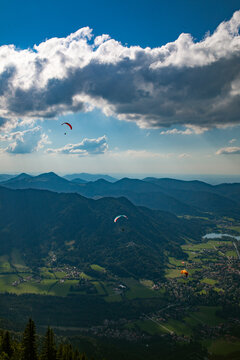 Aerial view of paragliders soaring over the mountainous landscape near the Konigssee lake with green valleys and forests in Schonau am Konigssee, Bavaria, Germany.