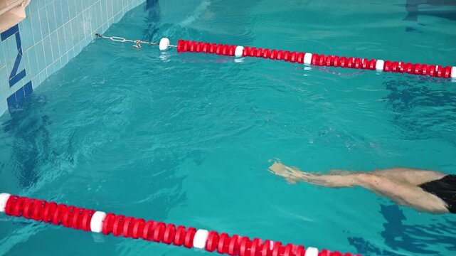 Woman performs backstroke turn in swimming pool near wall. Sport video captures rotation, leg tuck, and transition phase during lap training and competitive swimming practice