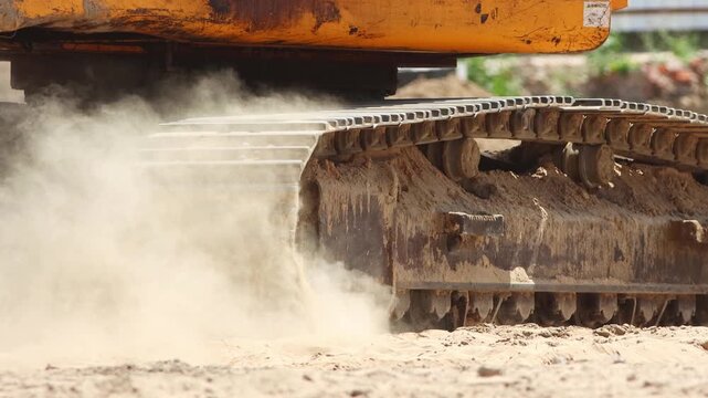 Excavator tracks moving on sand creating dust