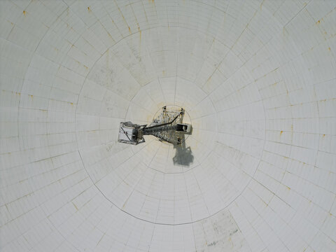 Aerial view of a large radio telescope dish with a central receiver structure and white paneling in the United Kingdom.