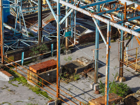 Aerial view of a weathered industrial chemical plant featuring rusted metal frameworks, concrete platforms, and overgrown vegetation in the United Kingdom.