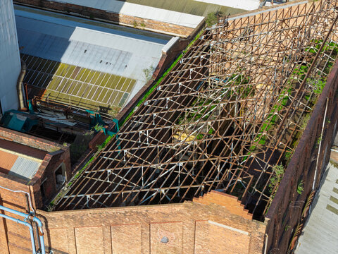 Aerial view of an old industrial chemical plant with a partially collapsed roof structure, exposed steel trusses, and brick walls in the United Kingdom.