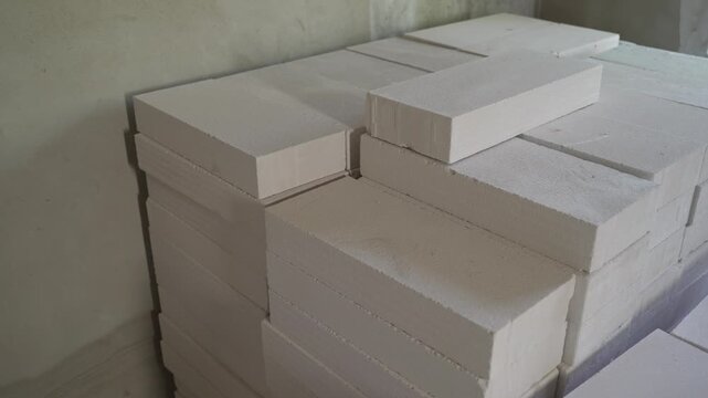 Slow pan shot of stacked white lightweight concrete blocks. Building materials for house construction are stored in a room. Close up view of new bricks for building a wall
