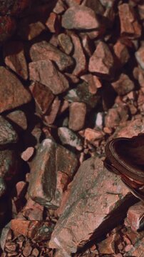 A worn shoe is resting on a rocky surface at a construction site. The rocks are irregular and vary in size and shape. The setting shows an unfinished area of work.