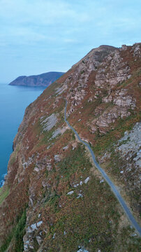 Aerial view of the rugged coastal cliffs and winding road at the Valley of Rocks, featuring dramatic rock formations and the calm sea in Lynton, England, United Kingdom.