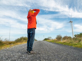 Person stands with arms wide open on gravel road. Red jacket and yellow hat contrast with blue sky. Feels freedom, peace, or adventure. Great for travel, wellness, or outdoor lifestyle themes. © mark_gusev