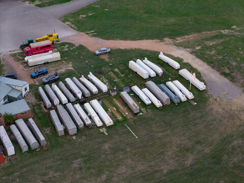 Aerial view of numerous white glider trailers parked in rows on a grassy field next to a building and several parked cars in the United Kingdom.