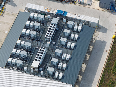 Aerial view of industrial rooftop with multiple HVAC cooling units and ventilation systems arranged in rows on a metal roof, United Kingdom.