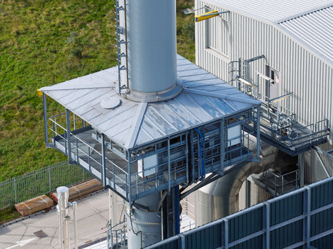 Aerial view of an industrial chimney stack with a metal platform and corrugated metal building in the United Kingdom.