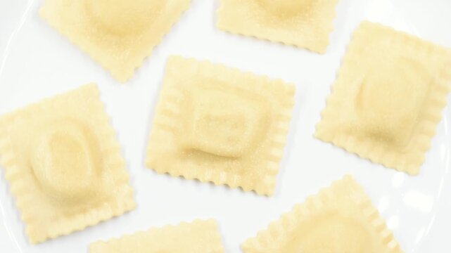 fresh Ravioli stuffed with ricotta cheese and asparagus, uncooked Italian egg pasta, close-up on a white plate, rotating video.