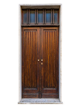 Antique dark brown wooden double entrance door, featuring vertical grooved panels, round brass doorknobs and glass transom window overhead, framed by light stone portal isolated 