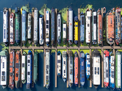 Aerial view of Saul Junction Marina with colorful narrowboats moored in parallel rows along wooden pontoons on the calm canal water in Frampton on Severn, England, United Kingdom.
