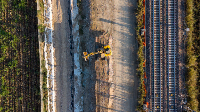 Aerial view of an excavator working on a new railway construction project with tracks and dirt paths in Milan, Lombardy, Italy.