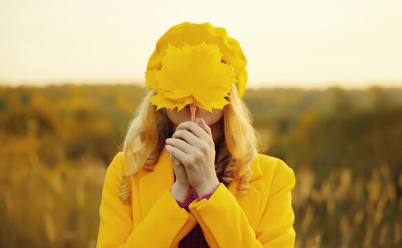 Happy woman having fun with yellow leaves in autumn park, nature background