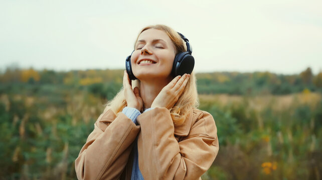 young woman enjoying listening to music in headphones outdoors in autumn