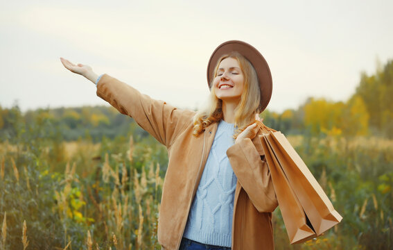 happy woman standing with shopping bag in autumn park, fashionable girl smiling outdoors