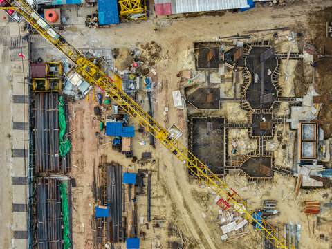 Aerial view of a construction site featuring a large yellow tower crane, foundation work with steel rebar, and various building materials in Samarinda, East Kalimantan, Indonesia.