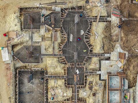 Aerial view of construction site foundation with steel rebar grids, concrete forms, and workers in hard hats at a building project in Samarinda, East Kalimantan, Indonesia.