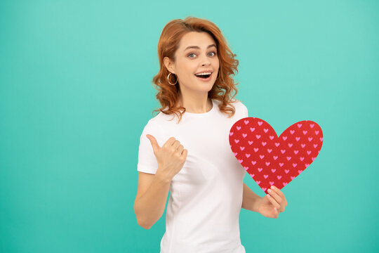 smiling young woman with red heart on blue background. thumb up