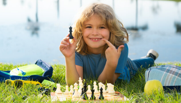 Kid playing chess game in backyard, laying on grass. Concentrated child play chess. Kid playing board game outdoor.