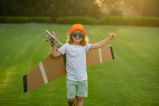 Happy kid playing with toy paper wings outdoors in summer field. Travel and kids vacation concept. Imagination and freedom.