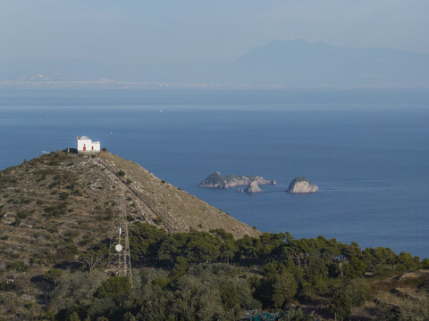 Aerial view of Punta Campanella with its historic lighthouse, Mediterranean scrub, and pine trees overlooking the Tyrrhenian Sea in Massa Lubrense, Campania, Italy.