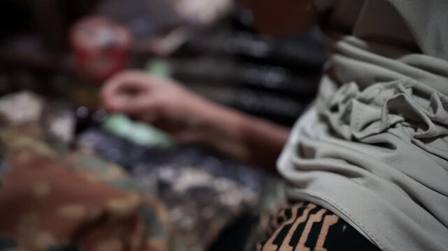 Close-up of artisan woman hand applying hot wax with canting tool for traditional batik making.