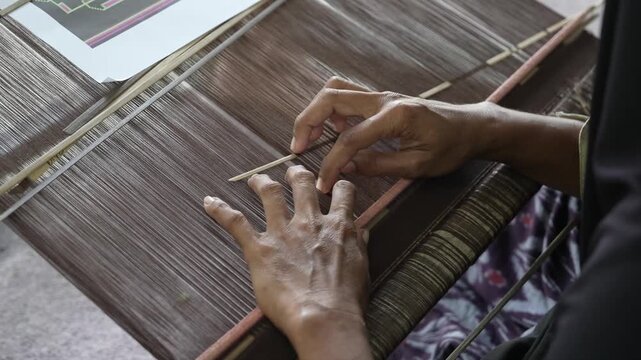 Close-up of elderly artisan hands arranging threads on traditional ikat weaving loom.