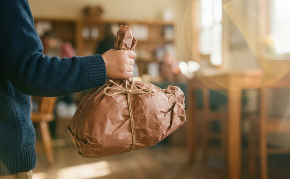 Young man holding a handmade paper parcel tied with string, representing eco-friendly packaging and sustainable delivery services in a rustic setting
