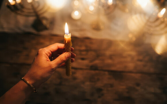 Woman holding a burning lit Hanukkah candle with menorah in background representing Jewish holiday tradition